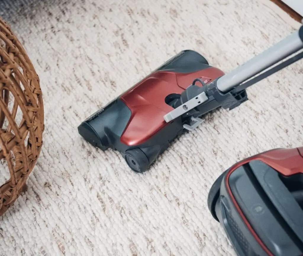 Close-up of a red and black vacuum cleaner head on a light-colored carpet next to a wicker basket, showcasing deep cleaning efficiency.