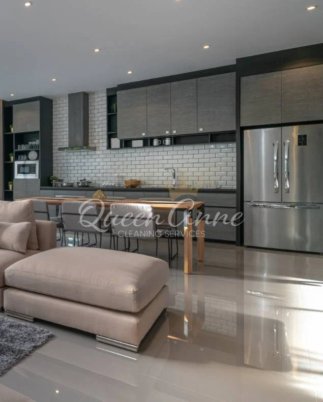 Modern kitchen and living area with stainless steel appliances, gray cabinets, and a cozy beige sofa. A dining table with chairs is positioned near the kitchen island, making it easy to maintain cleanliness with house cleaning services near me.