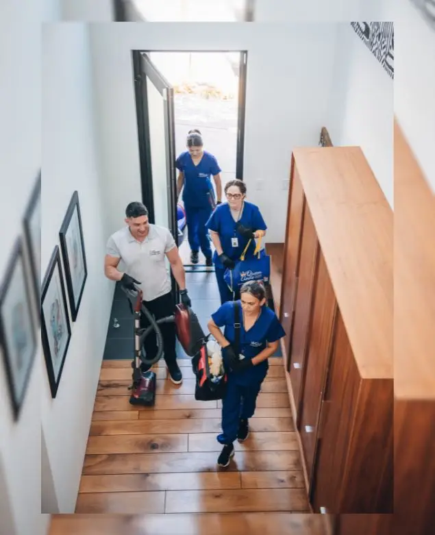 A maid service crew with cleaning equipment entering a house through the front door. The team consists of three professionals dressed in uniform, ready to provide top-notch house cleaning services near me.