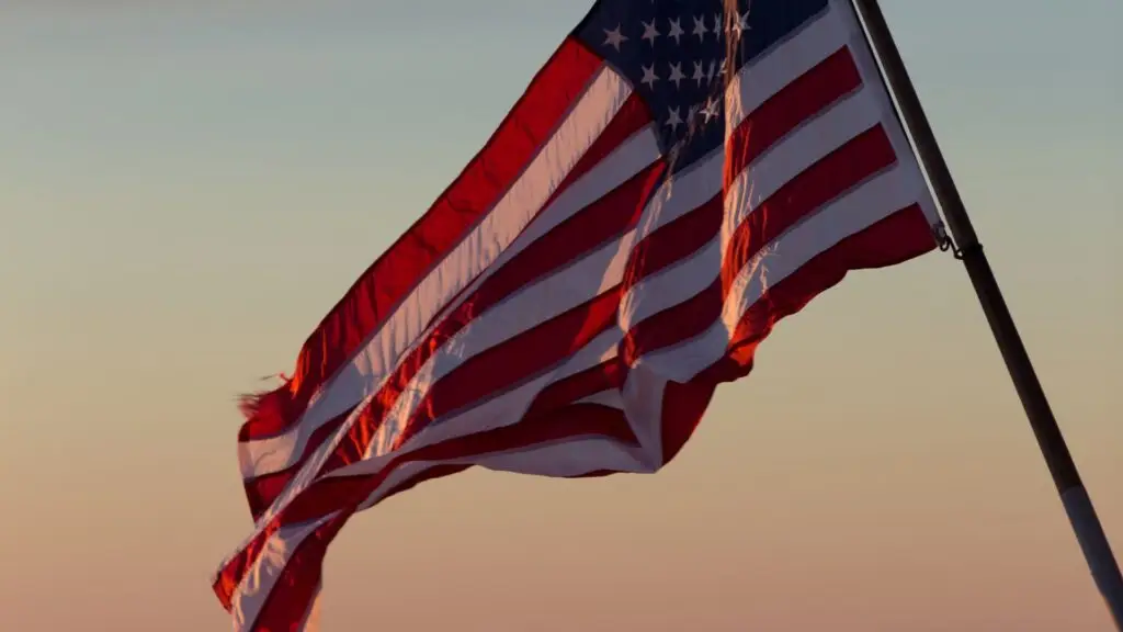 The United States flag waves in the wind against a sunset sky.