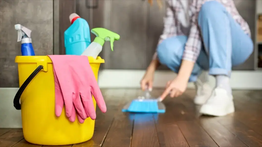 Yellow bucket with cleaning supplies and gloves; person sweeping floor in background—perfect for tackling your basement cleaning checklist.