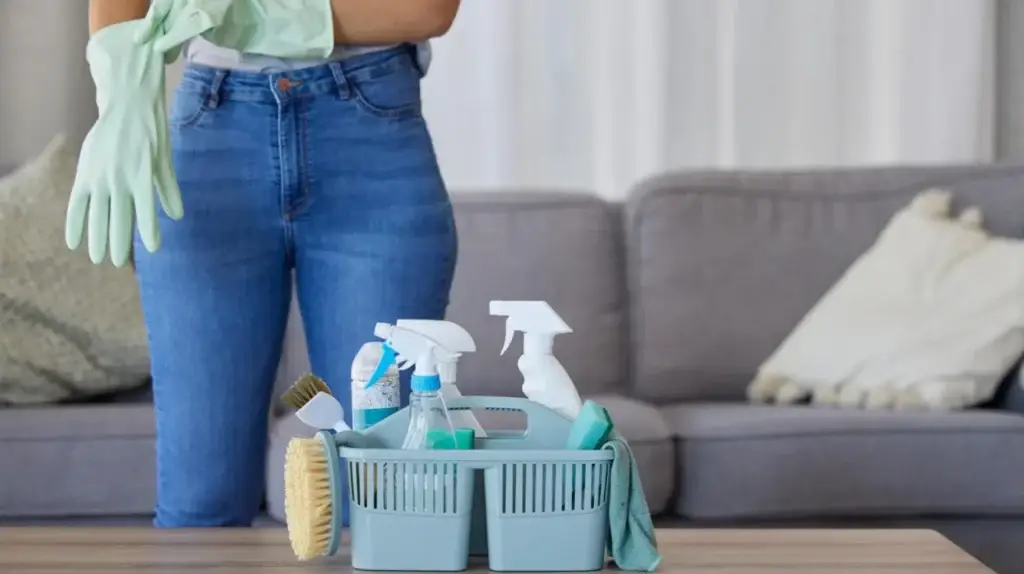 A person puts on gloves beside a cleaning caddy filled with supplies on a table in a cozy living room, representing a professional house cleaning service in Seattle.