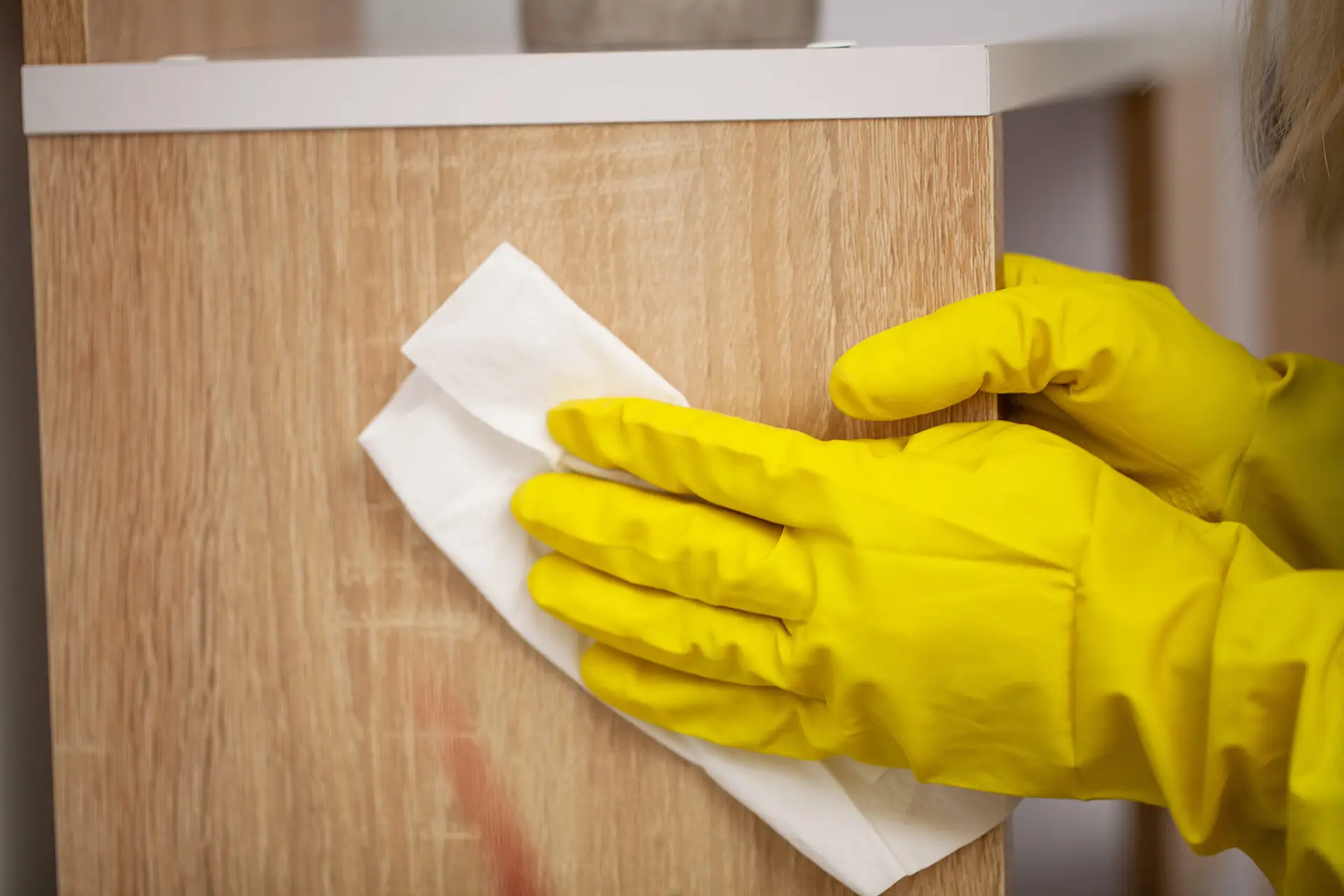 Hands in yellow gloves wiping a wooden surface with a white cloth, perfect for DIY furniture cleaning.