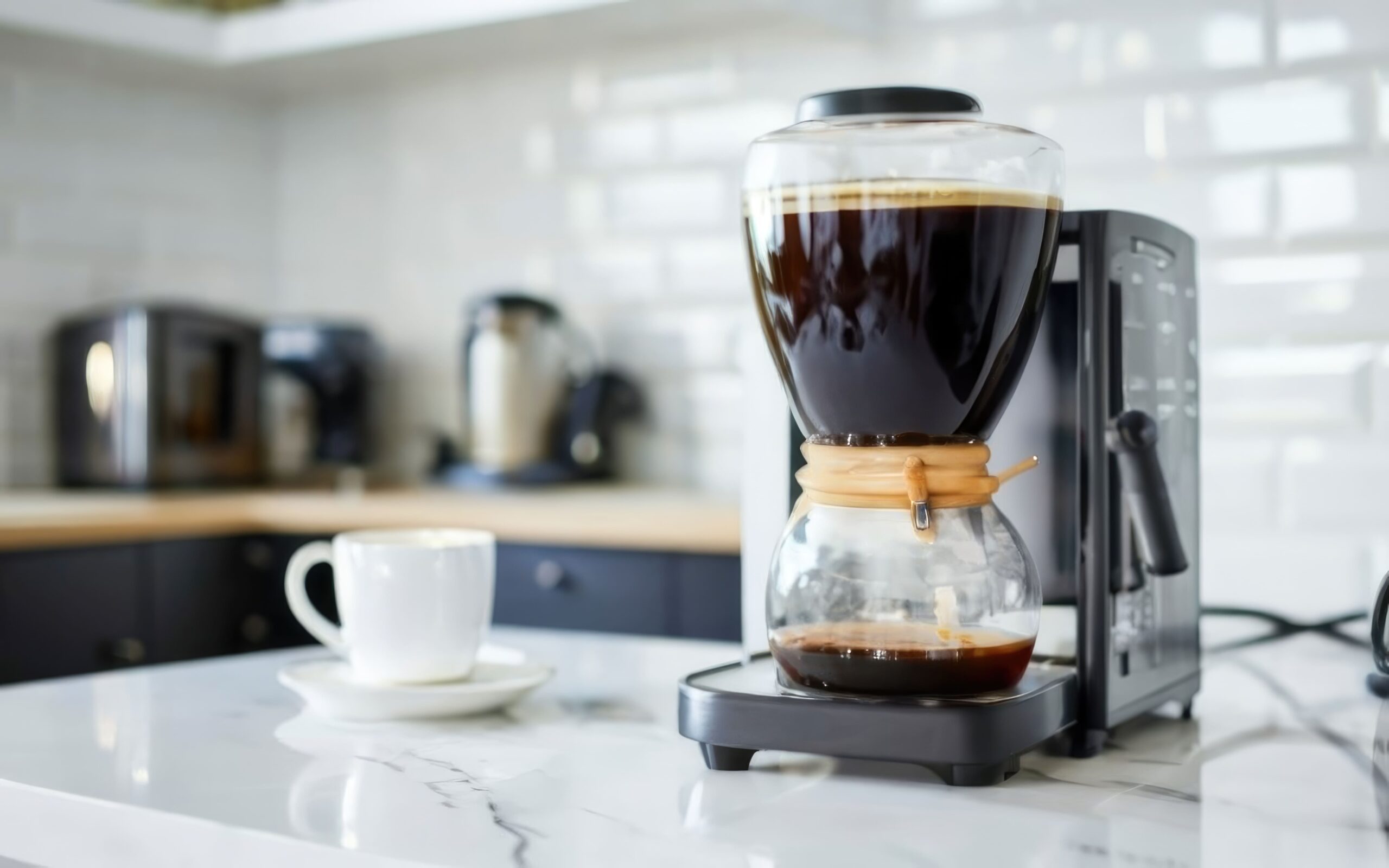 A coffee maker, kept spotless with regular coffee maker cleaning, brews coffee on a kitchen counter next to a white cup and saucer.