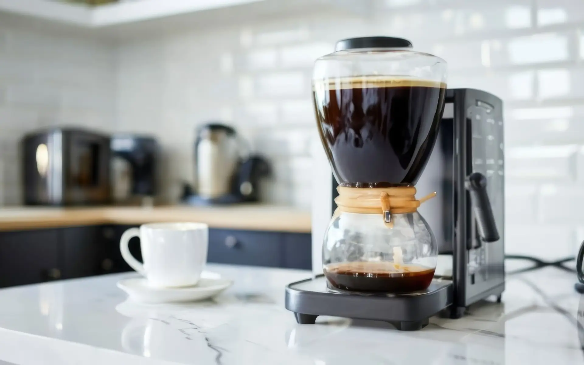 A coffee maker, kept spotless with regular coffee maker cleaning, brews coffee on a kitchen counter next to a white cup and saucer.